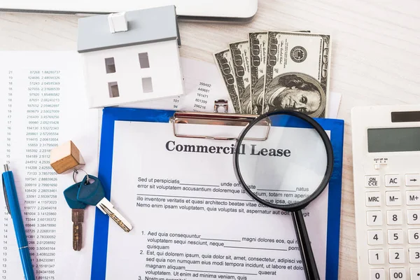 Vue du haut du document avec lettrage commercial sur presse-papiers près des clés, de l'argent, du modèle de maison, du stylo, de la calculatrice et de la loupe — Photo de stock