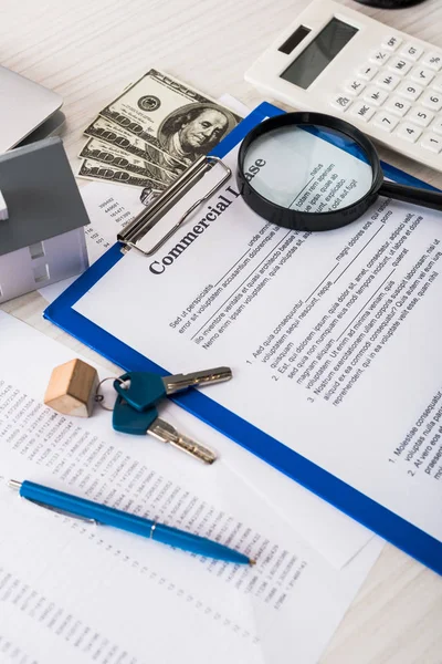 Documento con letras de arrendamiento comercial en portapapeles cerca de llaves, dinero, modelo de casa, pluma, calculadora y lupa - foto de stock