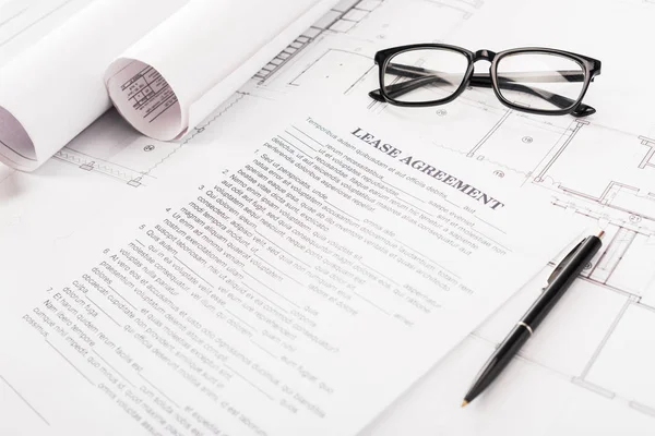 Documento con letras de contrato de arrendamiento cerca de gafas, planos y pluma en el escritorio - foto de stock