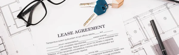 Панорамный снимок документа с договором аренды с надписью рядом со стеклами, чертежами и ключами на столе — стоковое фото