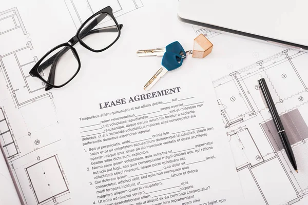 Top view of document with lease agreement lettering near glasses, blueprints and keys on desk — Stock Photo