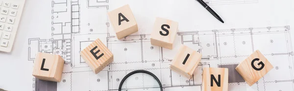 Panoramic shot of wooden cubes with leasing lettering on blueprints — Stock Photo