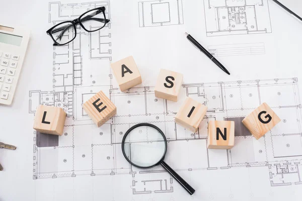 Top view of wooden cubes with leasing lettering near glasses, pen, magnifier and calculator on blueprints — Stock Photo