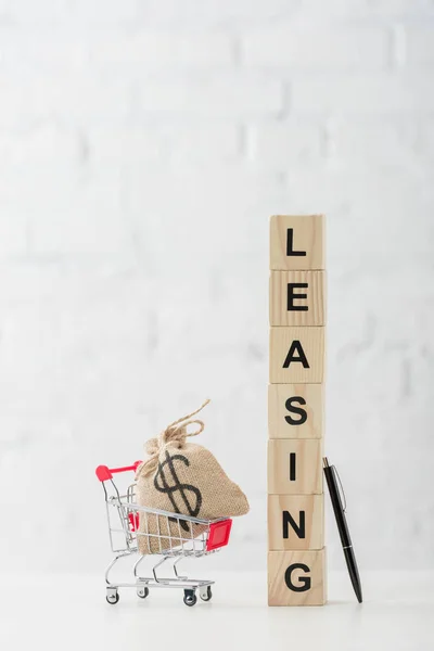 Cubes en bois avec lettrage de location près du chariot de jouets avec sac dollar sur blanc — Photo de stock