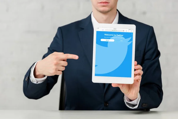 Cropped view of realtor in suit pointing with finger at digital tablet with twitter app on white — Stock Photo