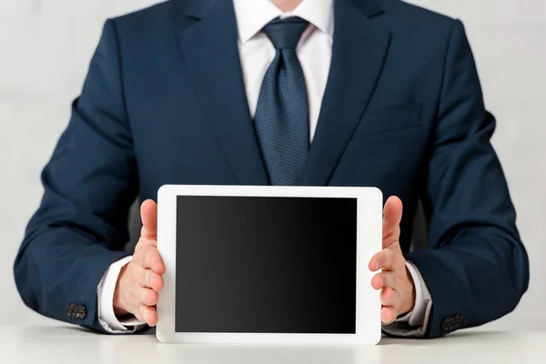 Обрезанный вид бизнесмена в костюме, держащего цифровой планшет с чистым экраном на белом — стоковое фото