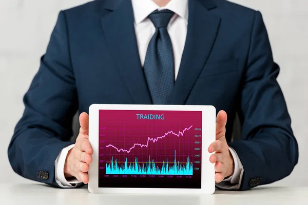 Recortado vista de hombre de negocios en traje celebración de tableta digital con cursos de comercio en la pantalla en blanco - foto de stock