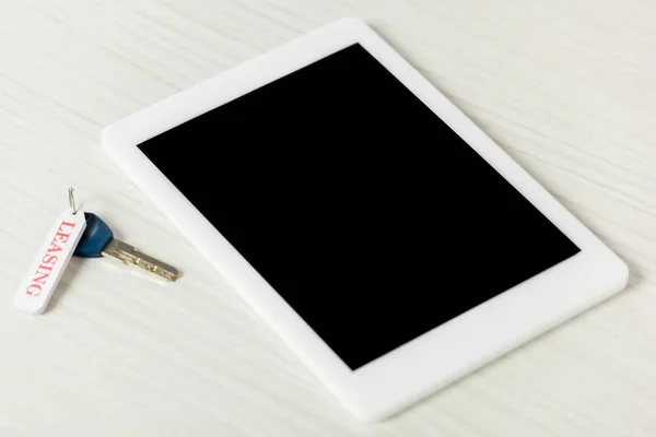 Clave con letras de arrendamiento cerca de tableta digital con pantalla en blanco en la mesa - foto de stock