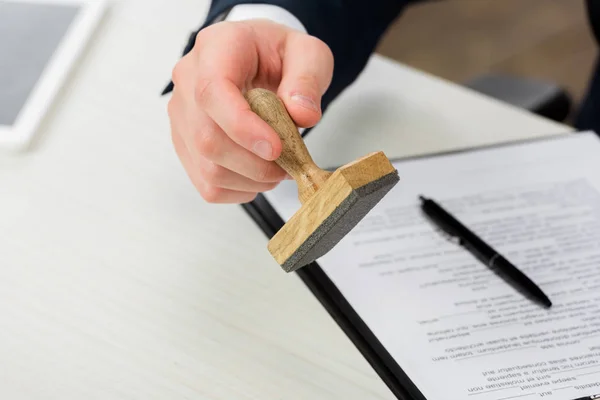 Vue recadrée de l'agent immobilier tenant le timbre près du presse-papiers et du stylo sur le bureau, concept de location — Photo de stock