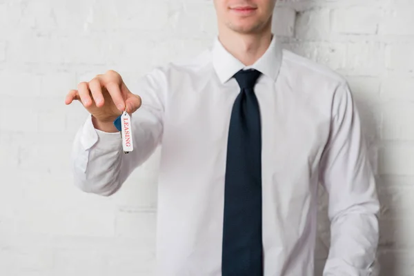 Cropped view of happy realtor in suit holding key with leasing lettering on white — Stock Photo