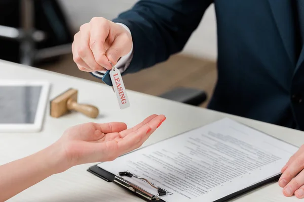 Ausgeschnittene Ansicht des Maklers, der Frau Schlüssel mit Leasing-Schriftzug übergibt — Stockfoto