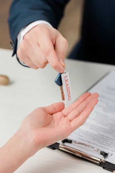 Ausgeschnittene Ansicht des Maklers, der Frau Schlüssel mit Leasing-Schriftzug übergibt — Stockfoto