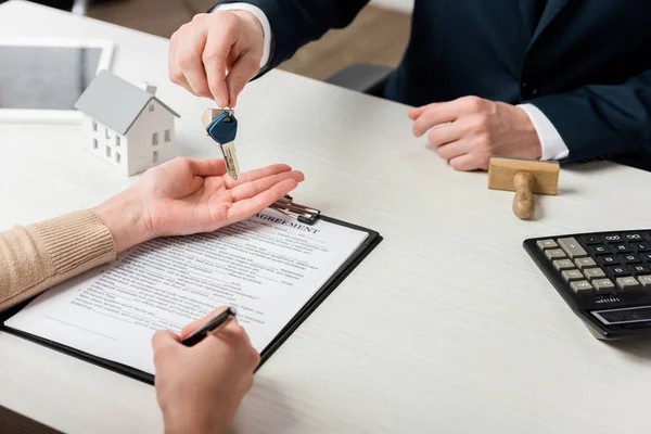 Vue recadrée de l'agent immobilier donnant la clé de la signature de l'accord femme, concept de location — Photo de stock