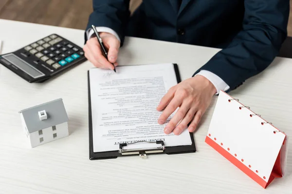 Vue recadrée de l'agent immobilier signant le contrat de location presque vierge calendrier, calculatrice et modèle de maison — Photo de stock