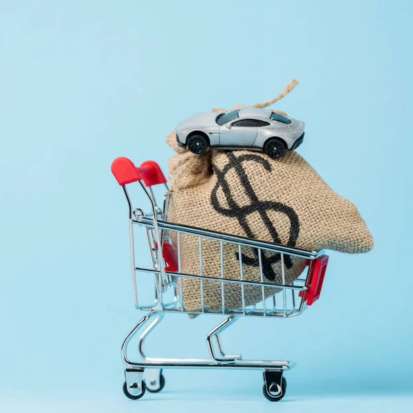 Carrinho de compras pequeno com saco de dólar e carro de brinquedo em azul, conceito de locação — Fotografia de Stock