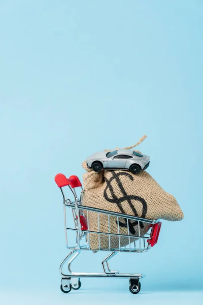 Kleiner Einkaufswagen mit Dollartasche und Spielzeugauto auf blau, Leasingkonzept — Stockfoto