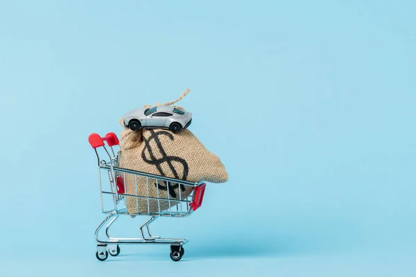 Piccolo carrello della spesa con borsa dollaro e macchinina su blu, concetto di leasing — Foto stock