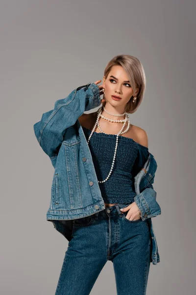 Atractiva mujer en chaqueta de mezclilla y jeans mirando hacia otro lado aislado en gris - foto de stock