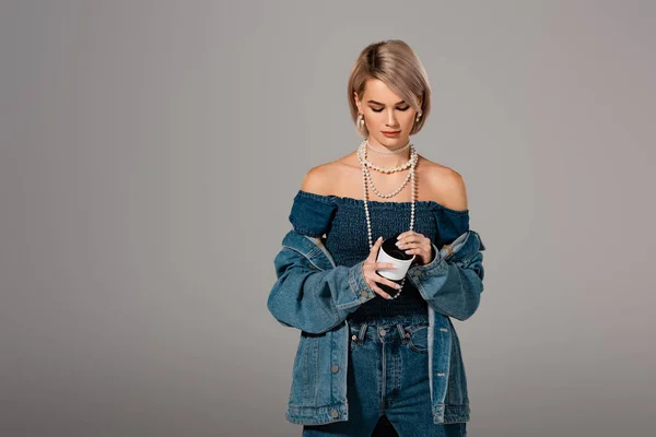 Jolie femme en jean veste tenant isolée tasse isolée sur gris — Photo de stock