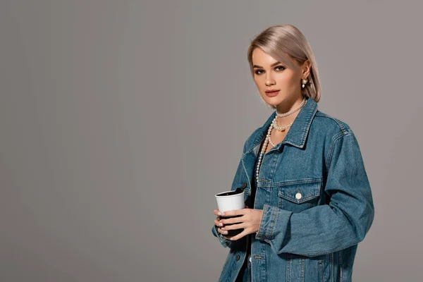 Attractive woman in denim jacket holding insulated mug and looking at camera isolated on grey — Stock Photo