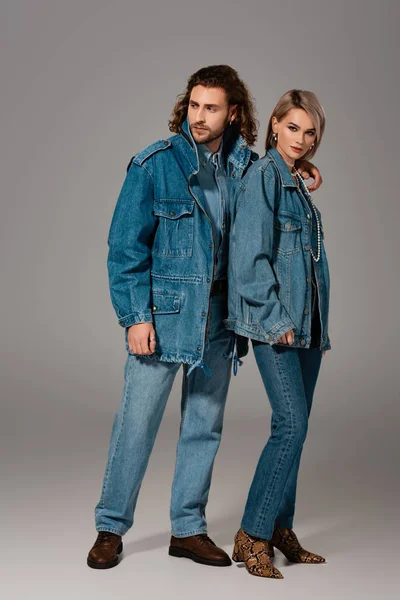 Стильный мужчина обнимает женщину в джинсовой куртке на сером фоне — стоковое фото