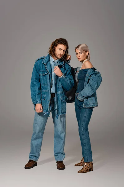 Stylish man and woman in denim jackets and jeans looking at camera on grey background — Stock Photo