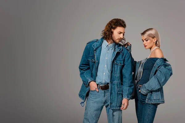 Elegante uomo e donna in giubbotti di jeans guardando verso il basso isolato sul grigio — Foto stock