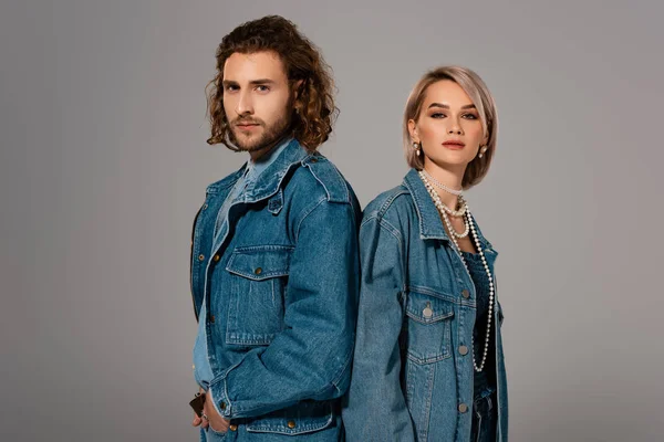 Back to back view of stylish man and woman in denim jackets looking at camera isolated on grey — Stock Photo
