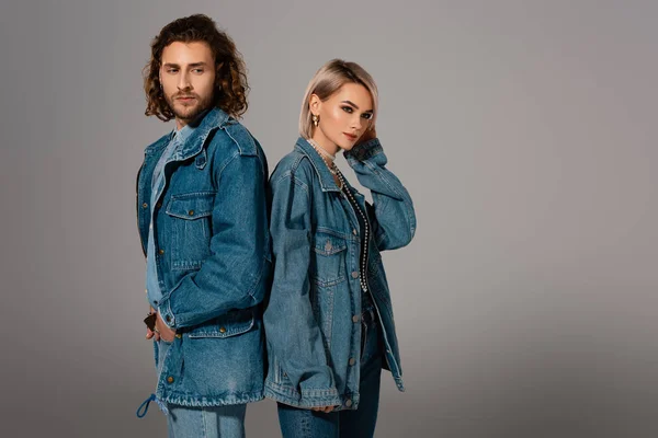 Назад на задній план стильний чоловік і жінка в джинсових куртках, що дивиться ізольовано на сірому — стокове фото