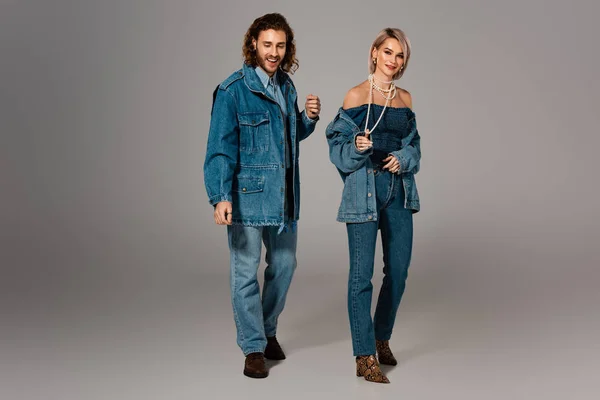 Улыбающиеся мужчина и женщина в джинсовых куртках и джинсах на сером фоне — стоковое фото