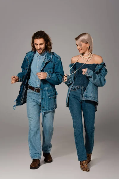 Smiling man and woman in denim jackets and jeans dancing on grey background — Stock Photo