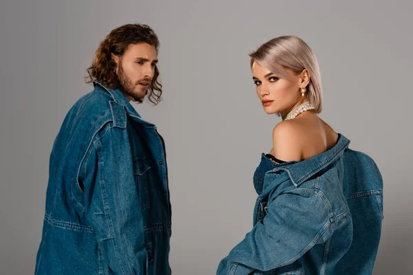 Homme élégant en veste en denim regardant femme attrayante isolée sur gris — Photo de stock