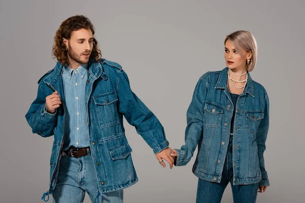 Стильный мужчина и женщина в джинсовых куртках, держась за руки изолированы на сером — стоковое фото