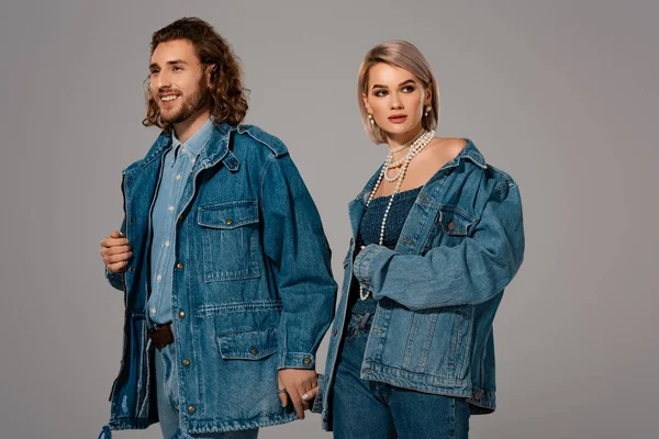 Hombre y mujer sonrientes en chaquetas de mezclilla tomados de las manos aislados en gris - foto de stock