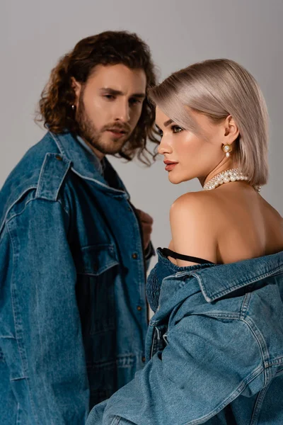 Hombre elegante mirando a la mujer en chaqueta de mezclilla aislado en gris - foto de stock