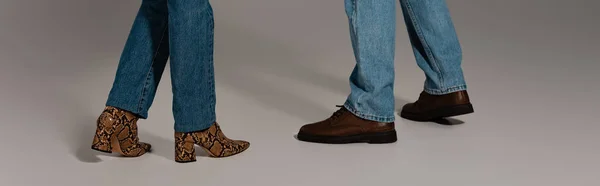 Cropped view of man and woman in denim jeans and shoes on grey background — Stock Photo