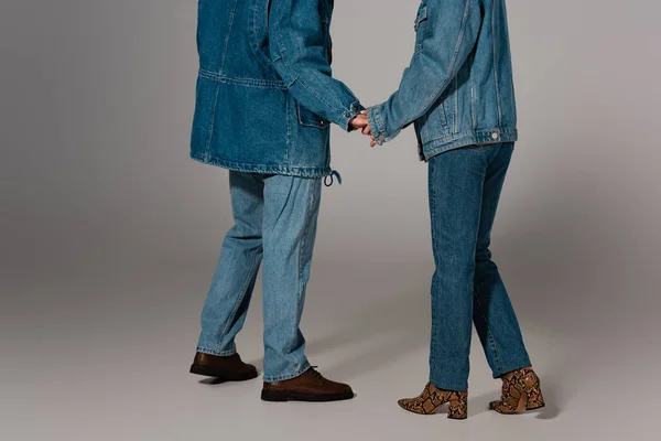 Vue recadrée de l'homme et de la femme élégants en vestes en denim et jeans tenant la main sur fond gris — Photo de stock