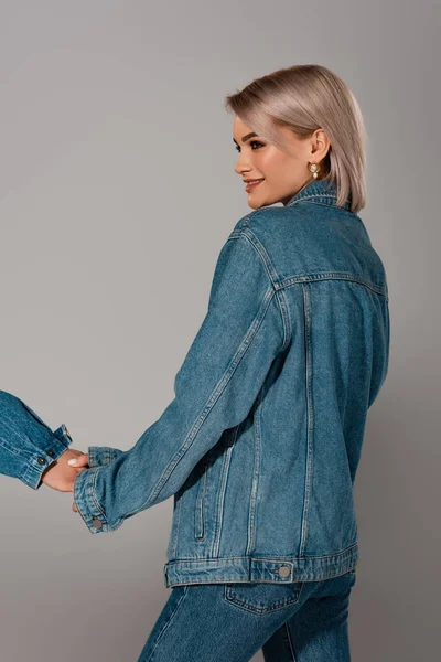 Обрезанный вид мужчины, держащегося за руки с улыбающейся женщиной в джинсовой куртке, изолированной на сером — стоковое фото