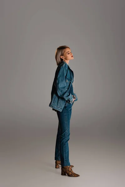 Side view of attractive woman in denim jacket and jeans looking away on grey background — Stock Photo