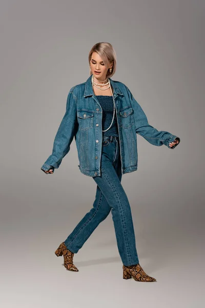 Atractiva mujer en chaqueta de mezclilla y jeans posando sobre fondo gris - foto de stock