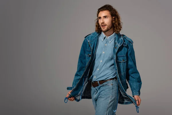 Красивий і стильний чоловік в джинсовій куртці і джинсах дивиться ізольовано на сірий — Stock Photo