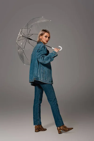 Attraktive Frau in Jeansjacke und Jeans mit Regenschirm auf grauem Hintergrund — Stockfoto