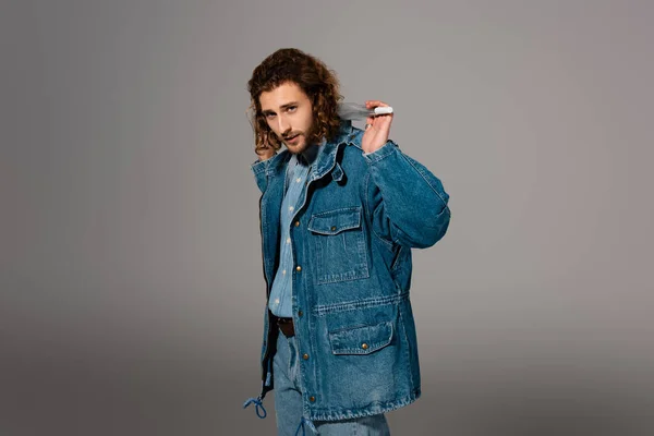 Schöner und stilvoller Mann in Jeansjacke und Jeans, Regenschirm isoliert auf grau — Stockfoto