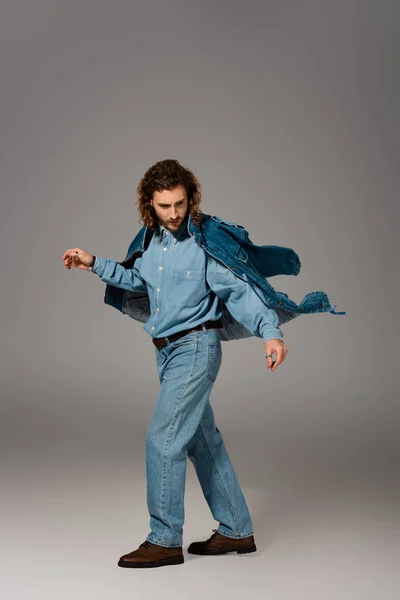 Hombre guapo y elegante en chaqueta de mezclilla y jeans posando sobre fondo gris - foto de stock