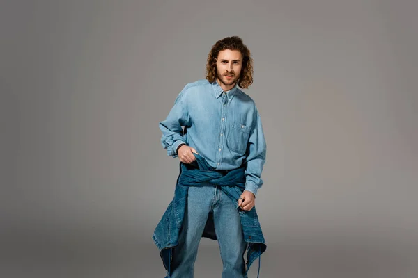 Homem bonito e elegante em camisa jeans e jeans olhando para a câmera isolada em cinza — Fotografia de Stock