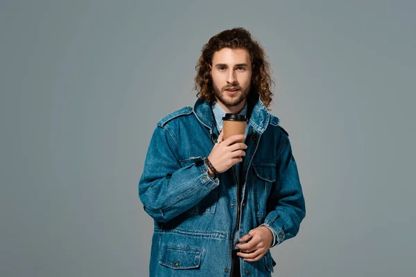 Hombre guapo y elegante en chaqueta de mezclilla sosteniendo taza de papel aislado en gris - foto de stock