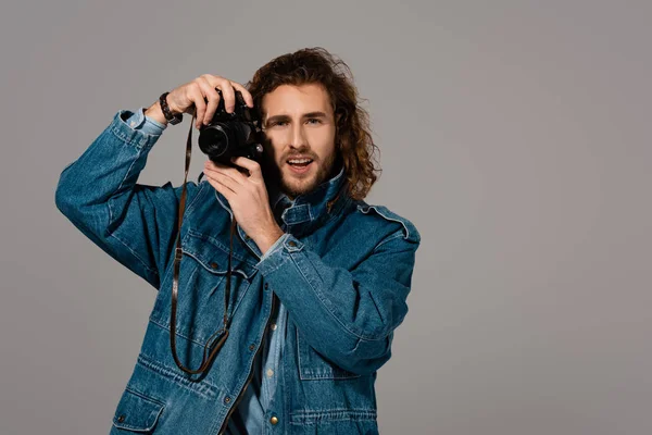 Красивый и стильный мужчина в джинсовой куртке с цифровой камерой, изолированной на сером — стоковое фото