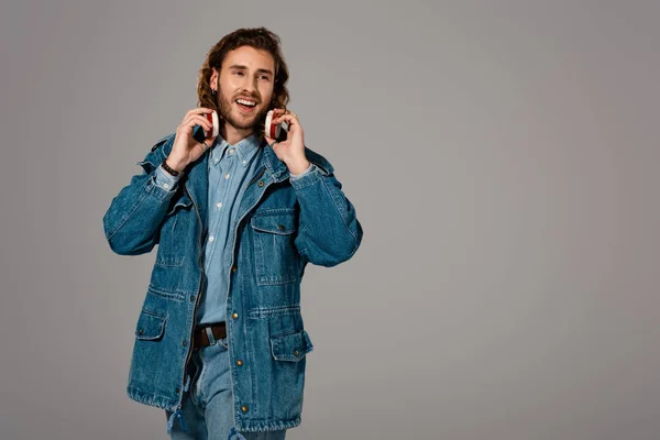 Bel homme souriant veste en denim et jeans avec écouteurs isolés sur gris — Photo de stock