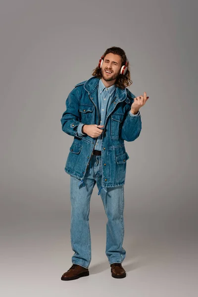 Homme beau et élégant en jean veste écouter de la musique avec écouteurs sur fond gris — Photo de stock