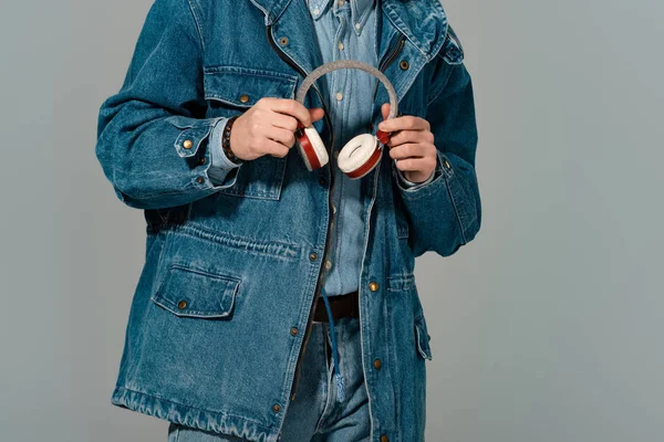 Vue recadrée de l'homme élégant en jean veste tenant écouteurs isolés sur gris — Photo de stock